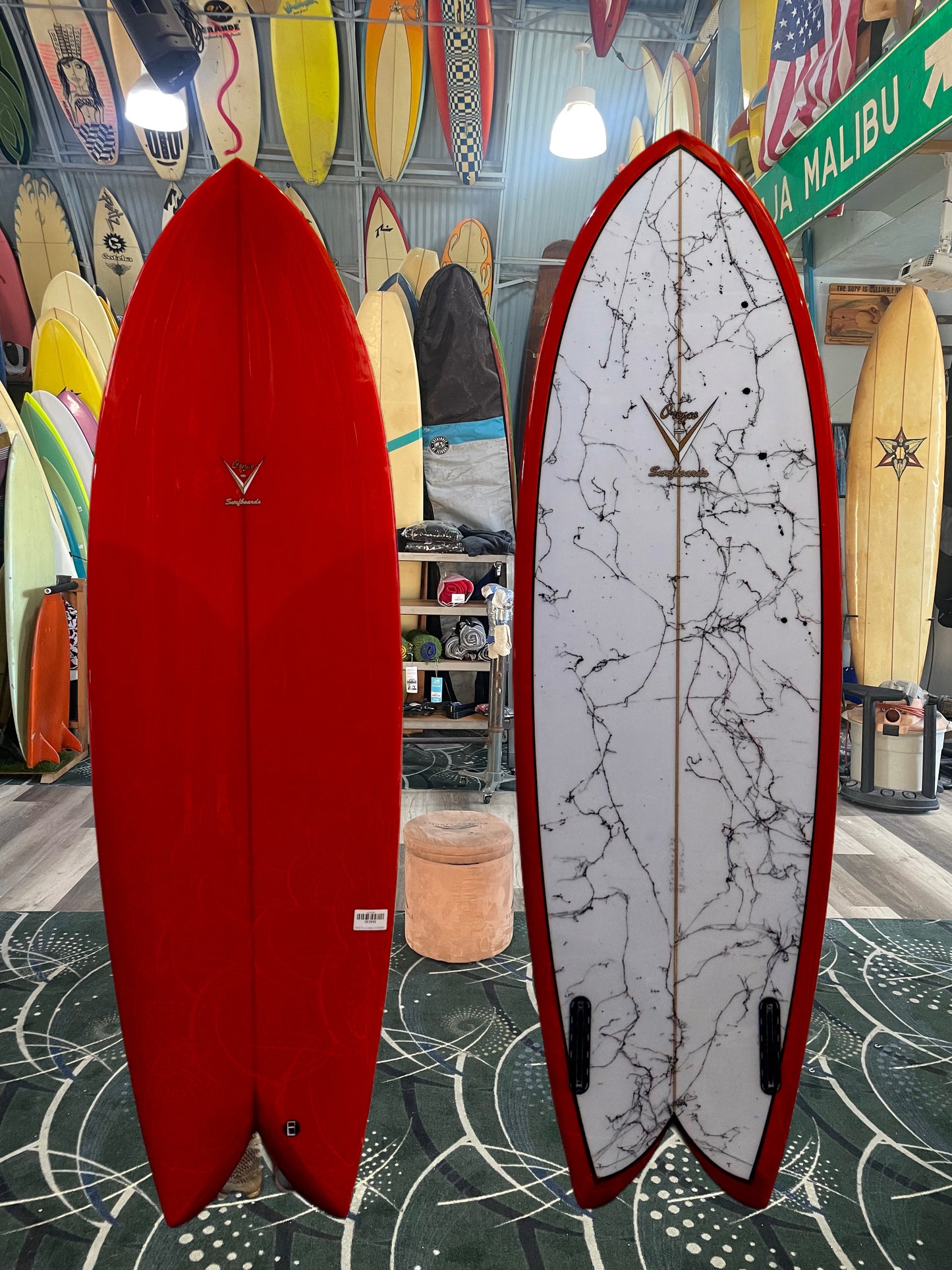 Two surfboards, one red and one with a white and black pattern, displayed indoors.