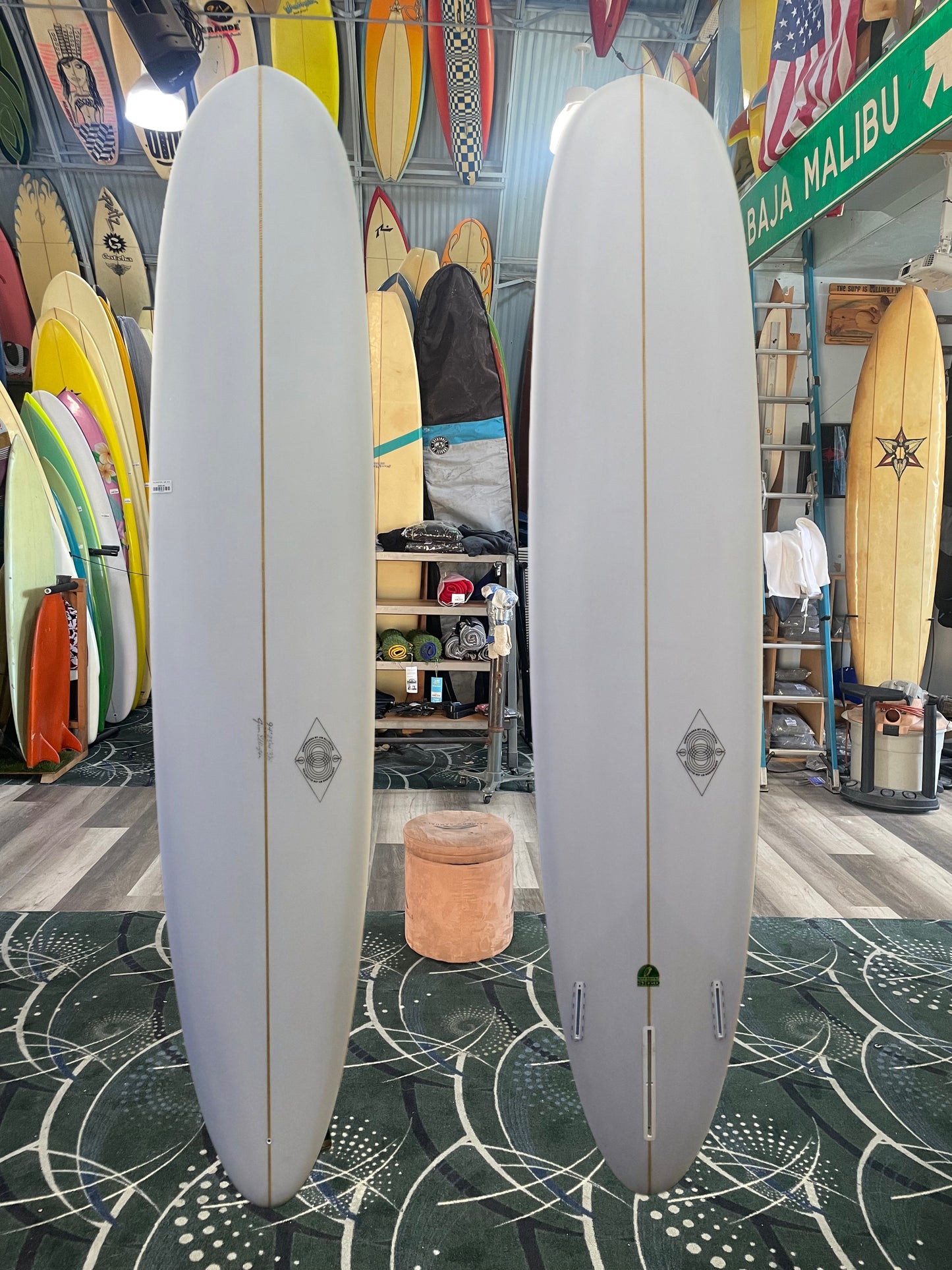 Two white surfboards on a green and black patterned floor with a store interior in the background.