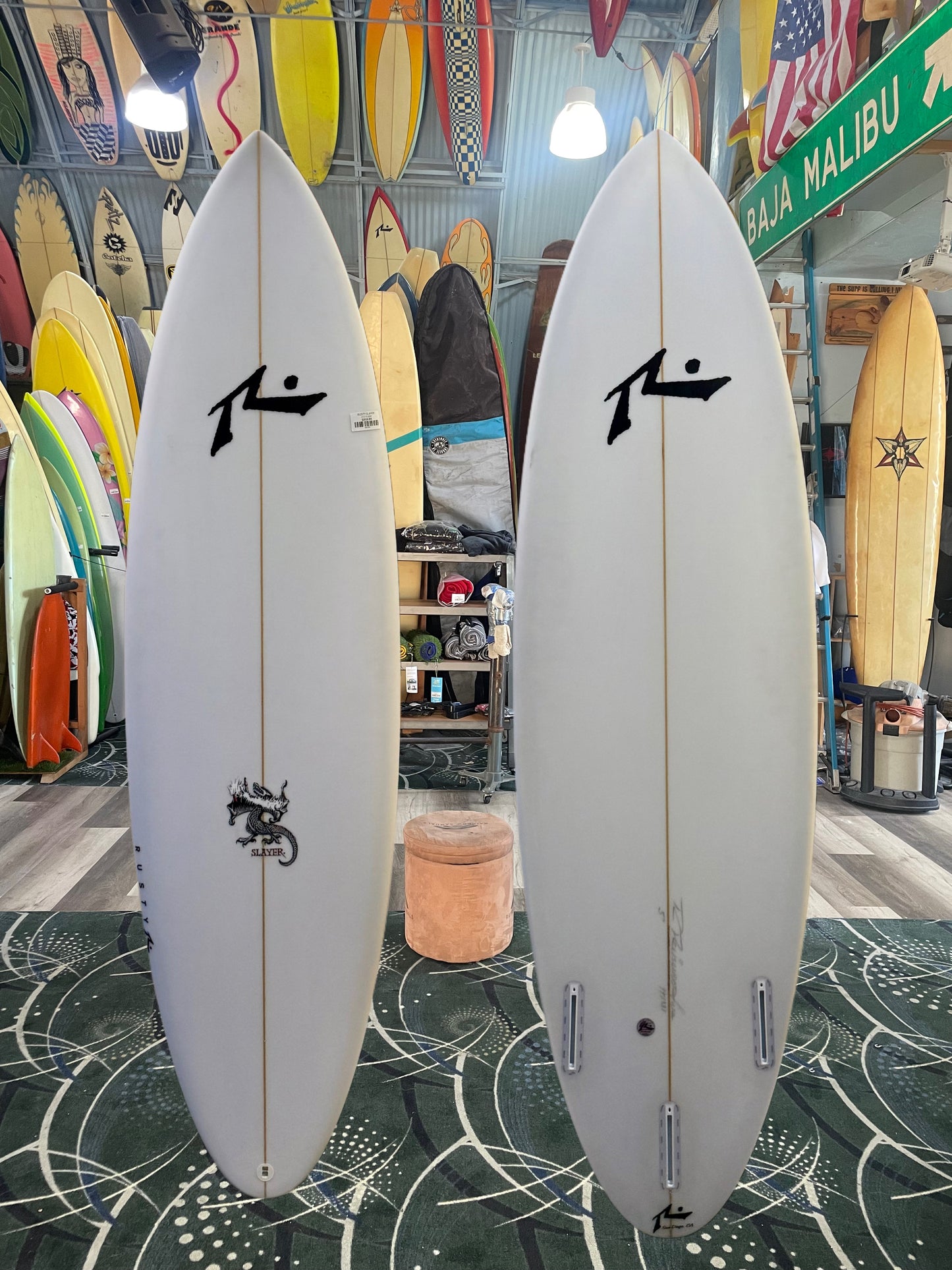 Two white surfboards with a logo on a patterned floor in a store setting.