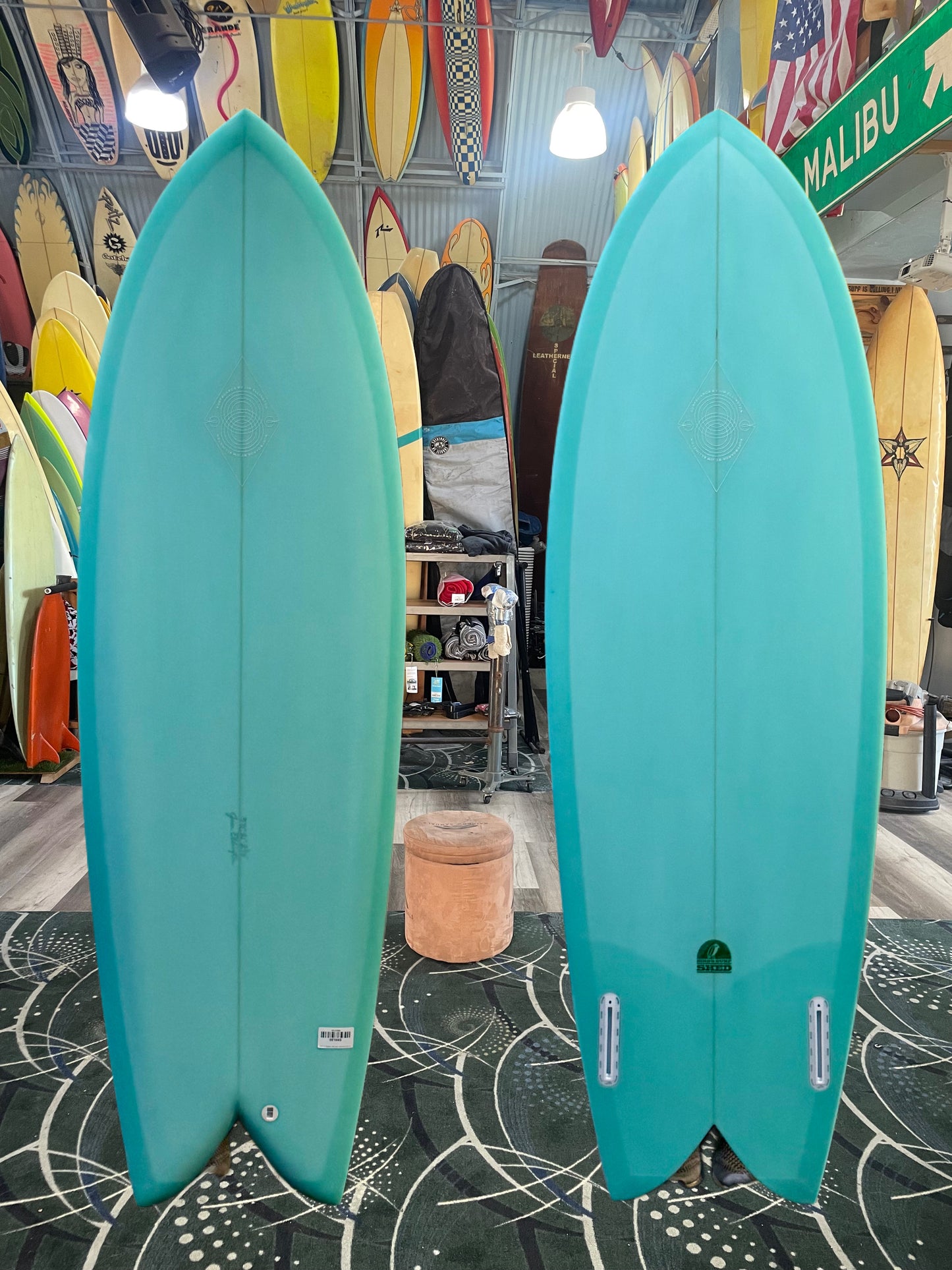 Two teal surfboards side by side in a store with various surfboards in the background.