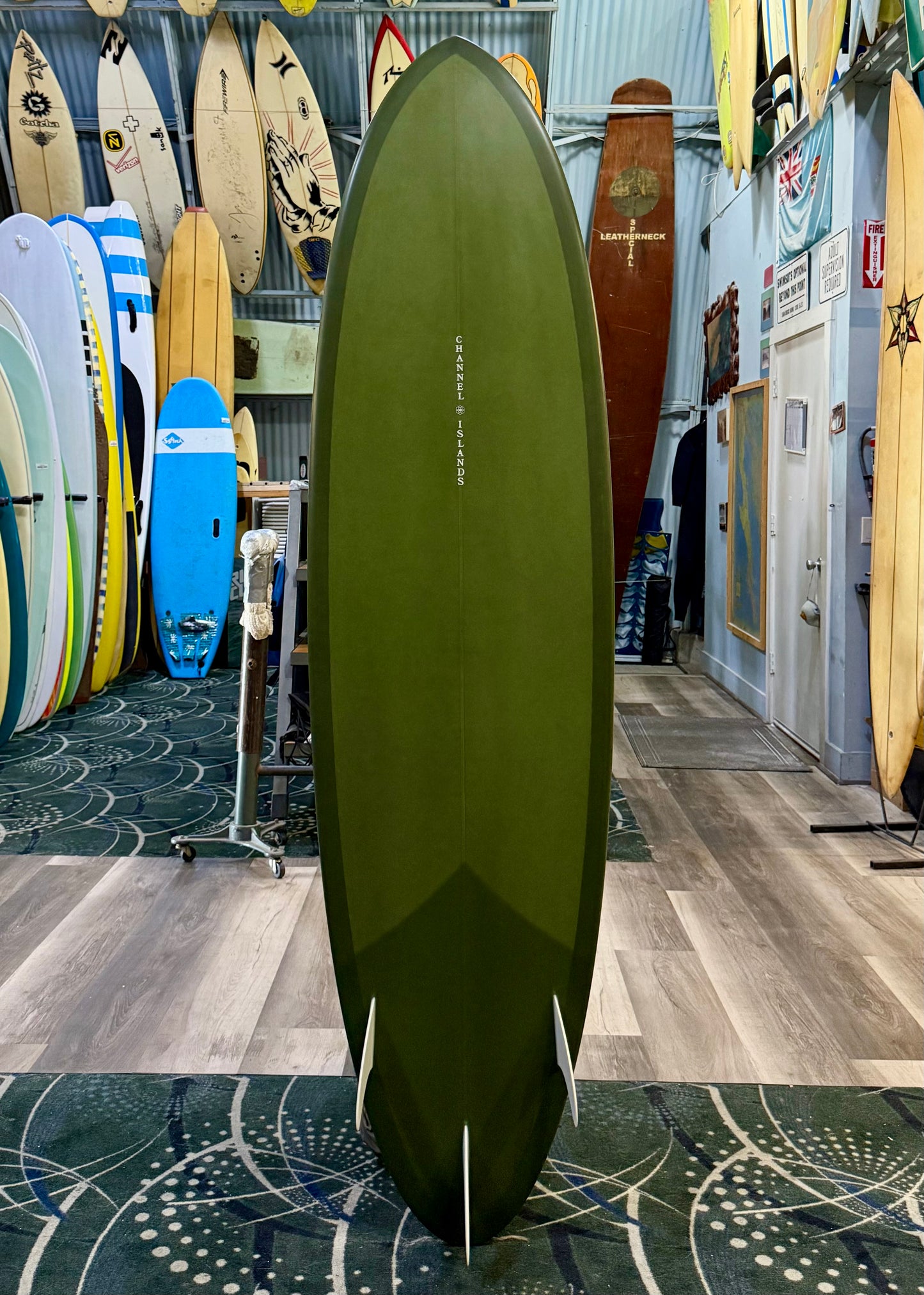 Green surfboard with fins on a wooden floor in a surfboard shop.