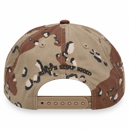 Back view of a desert camouflage snapback cap with 'BIRD'S SURF SHED' embroidered on the center panel, set against a plain white background.