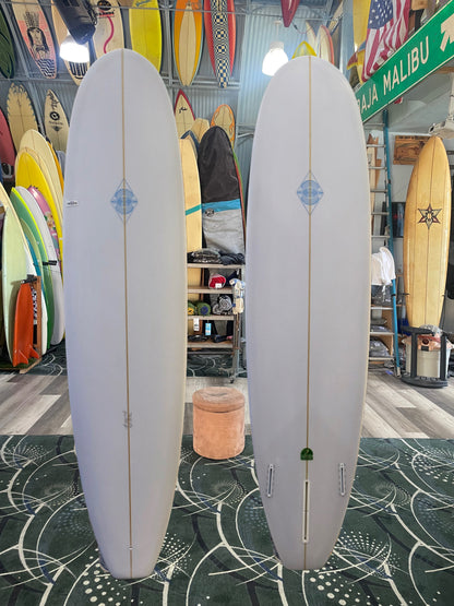 Two white surfboards with blue logos on a green patterned floor in a surf shop.