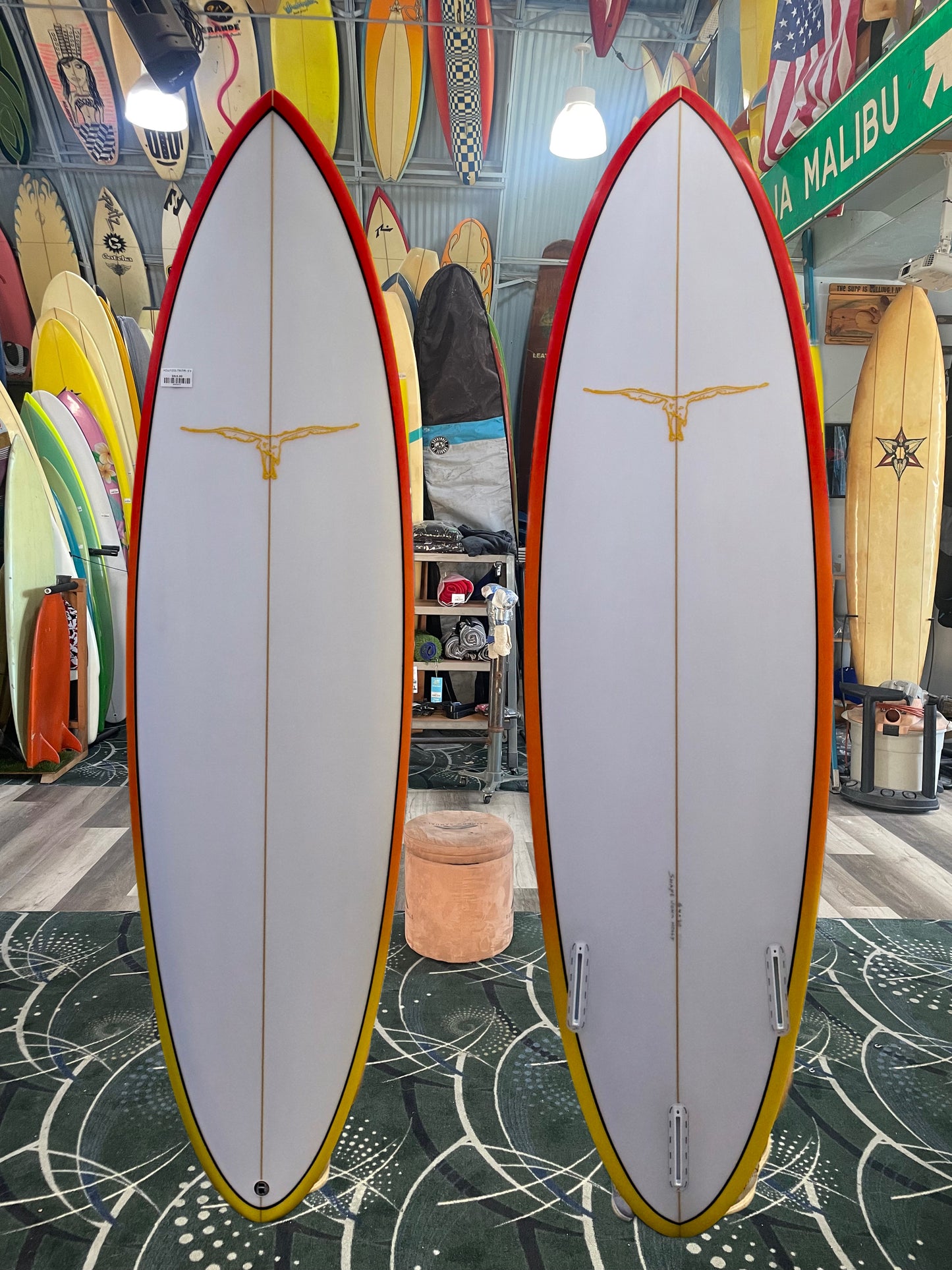 Two surfboards with a red and yellow design on a patterned floor, surrounded by various other surfboards.