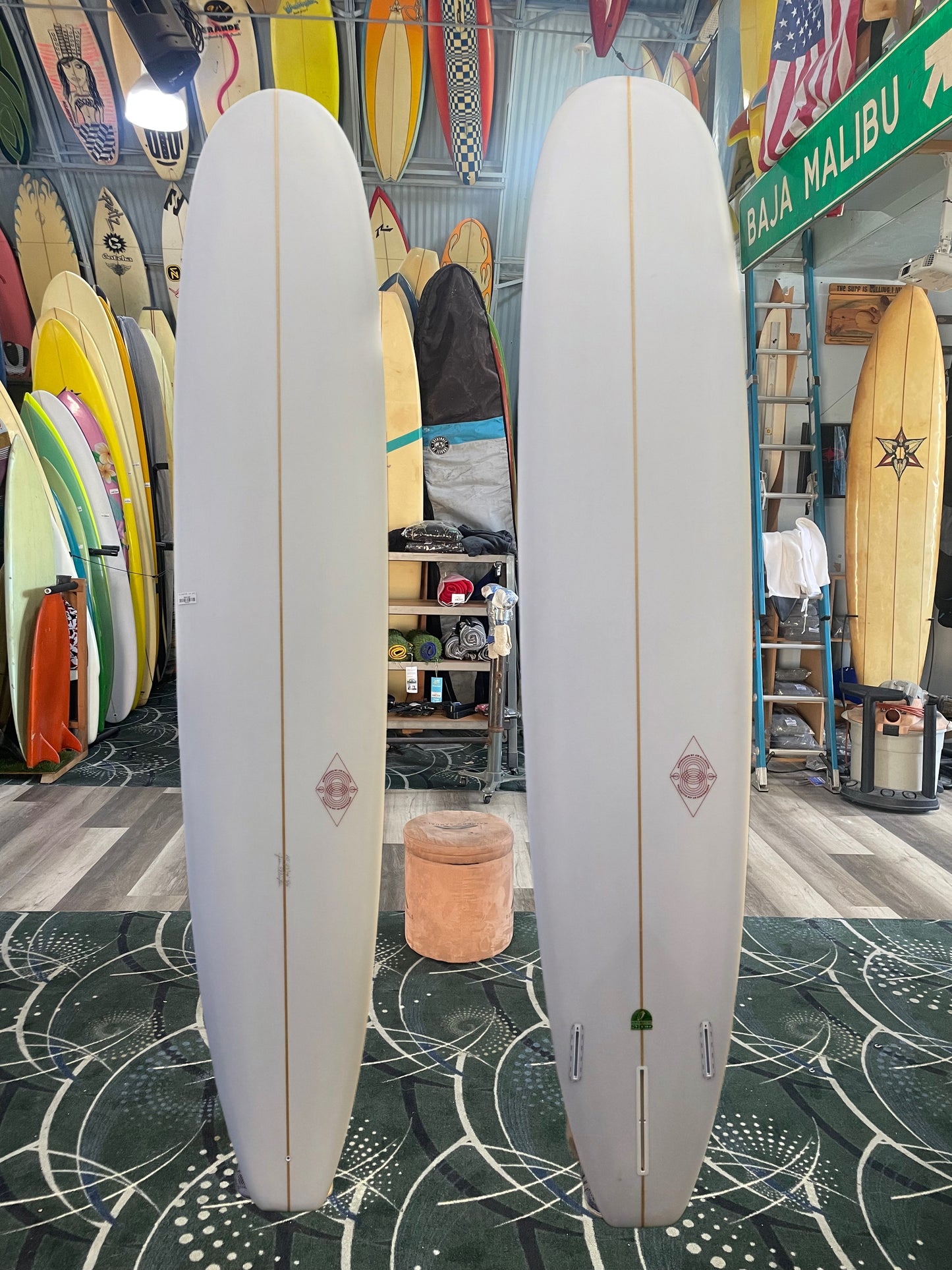 Two white surfboards with a logo on a green patterned floor in a store setting.