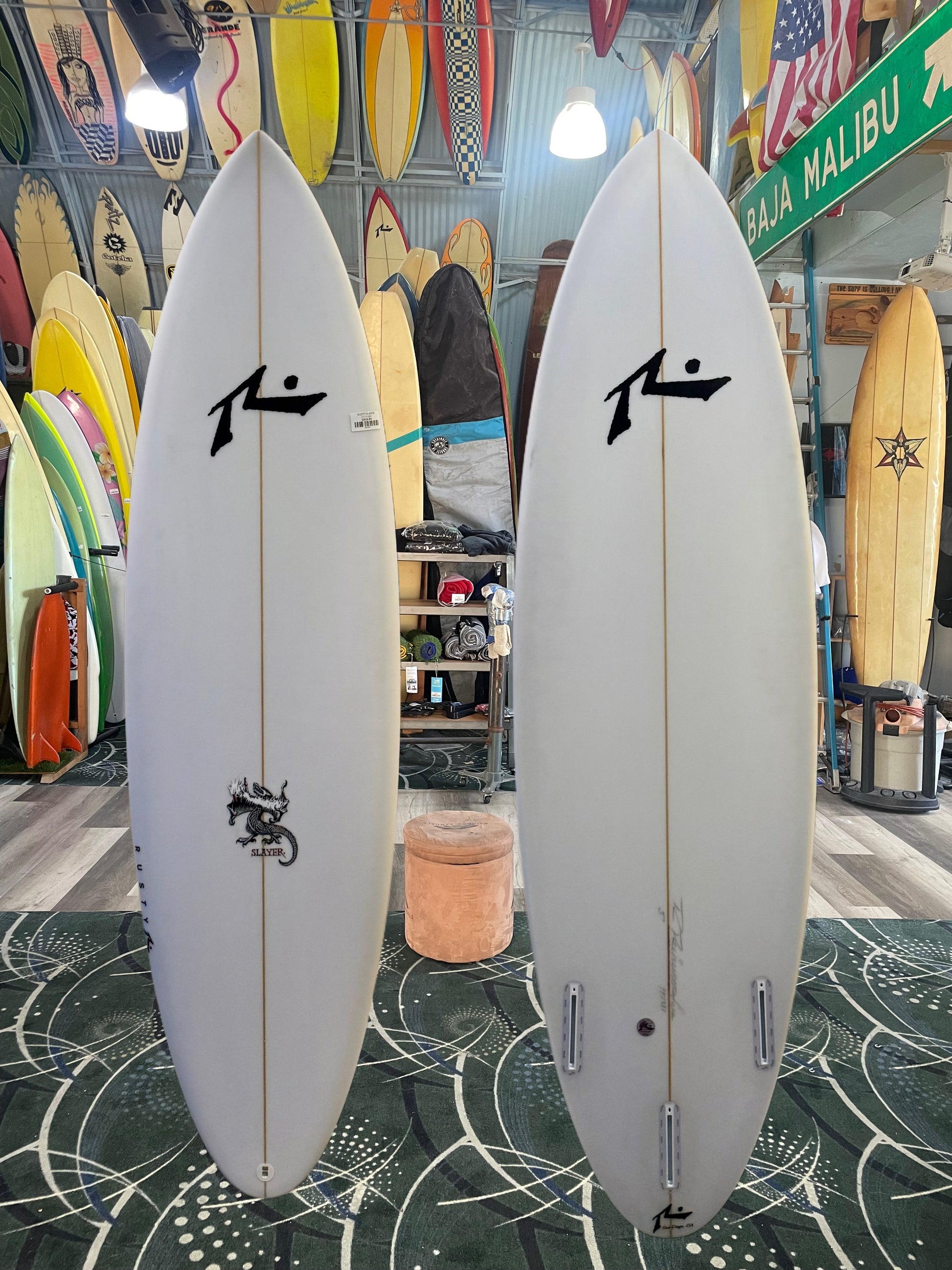 Two white surfboards with a logo on a patterned floor in a store setting.