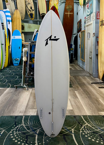 White surfboard with a black logo in a store setting with other surfboards.