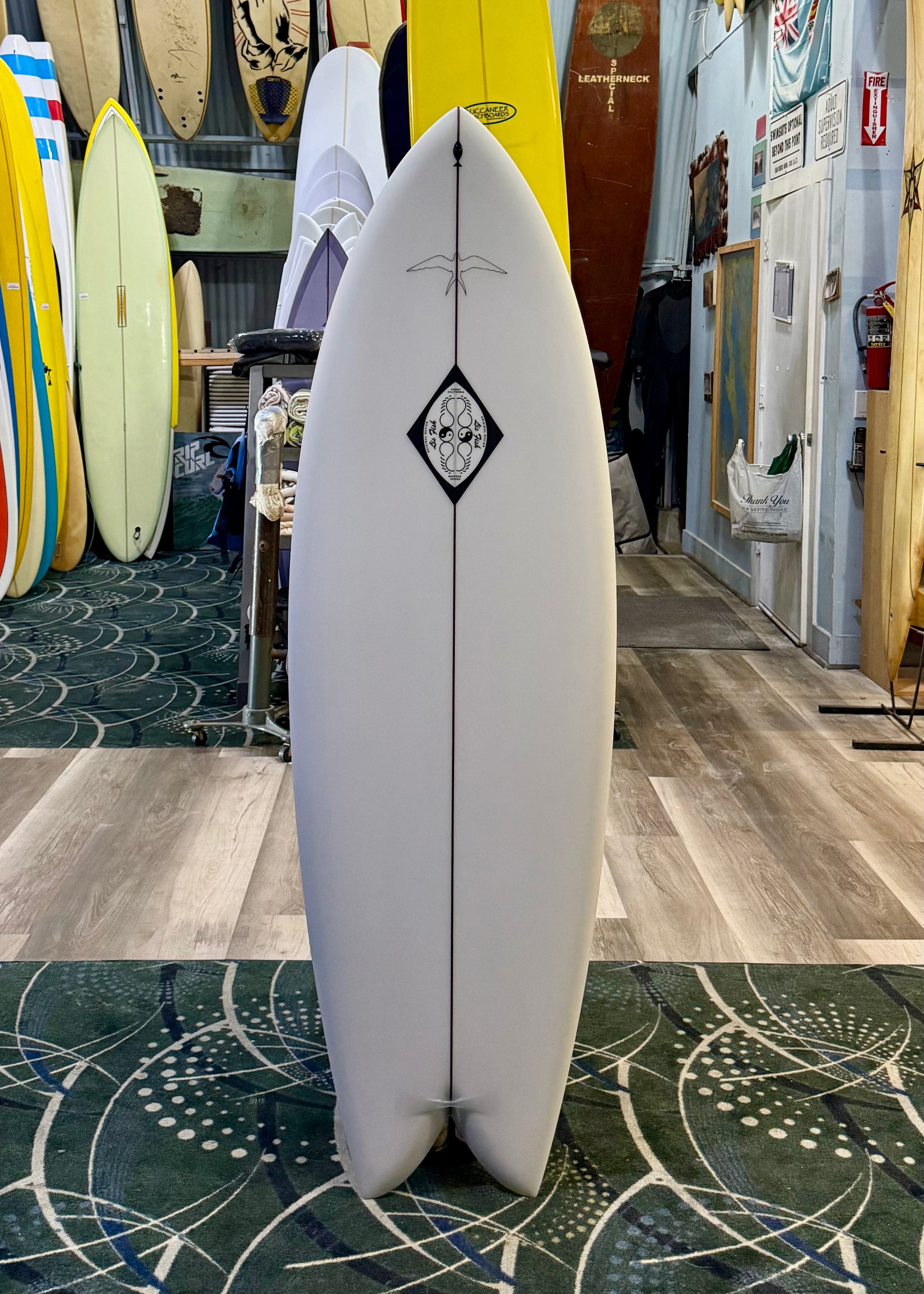 White surfboard with a black diamond design in a store setting with other surfboards.