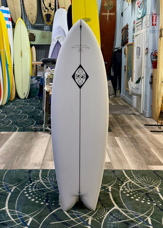 White surfboard with a black diamond design in a store setting with other surfboards.