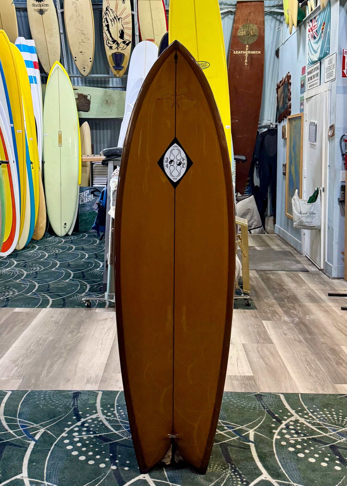 Brown surfboard with a logo on a tiled floor in a surf shop.