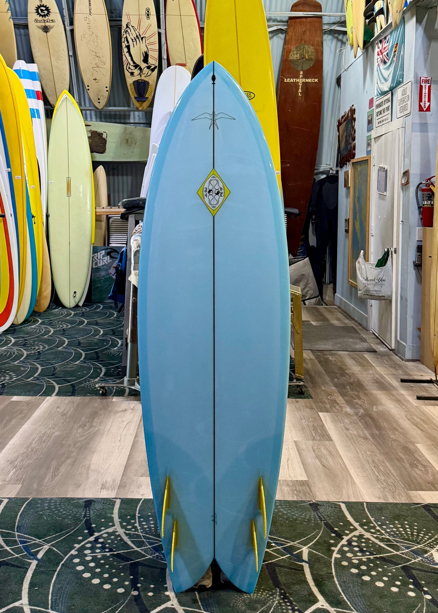 Blue surfboard with yellow fins in a surf shop with other boards in the background