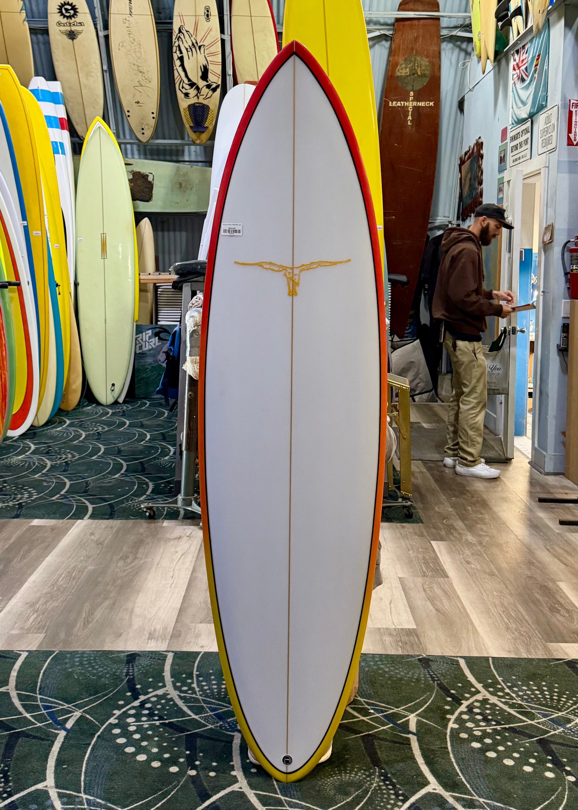 Surfboard with red and yellow accents displayed in a store with other surfboards in the background.