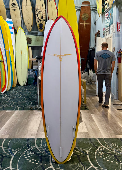 Surfboard with a red and yellow design in a surf shop with other boards and a person in the background.