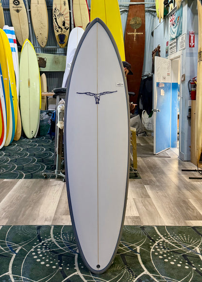 Surfboard with a design on a stand in a surf shop with various surfboards in the background.