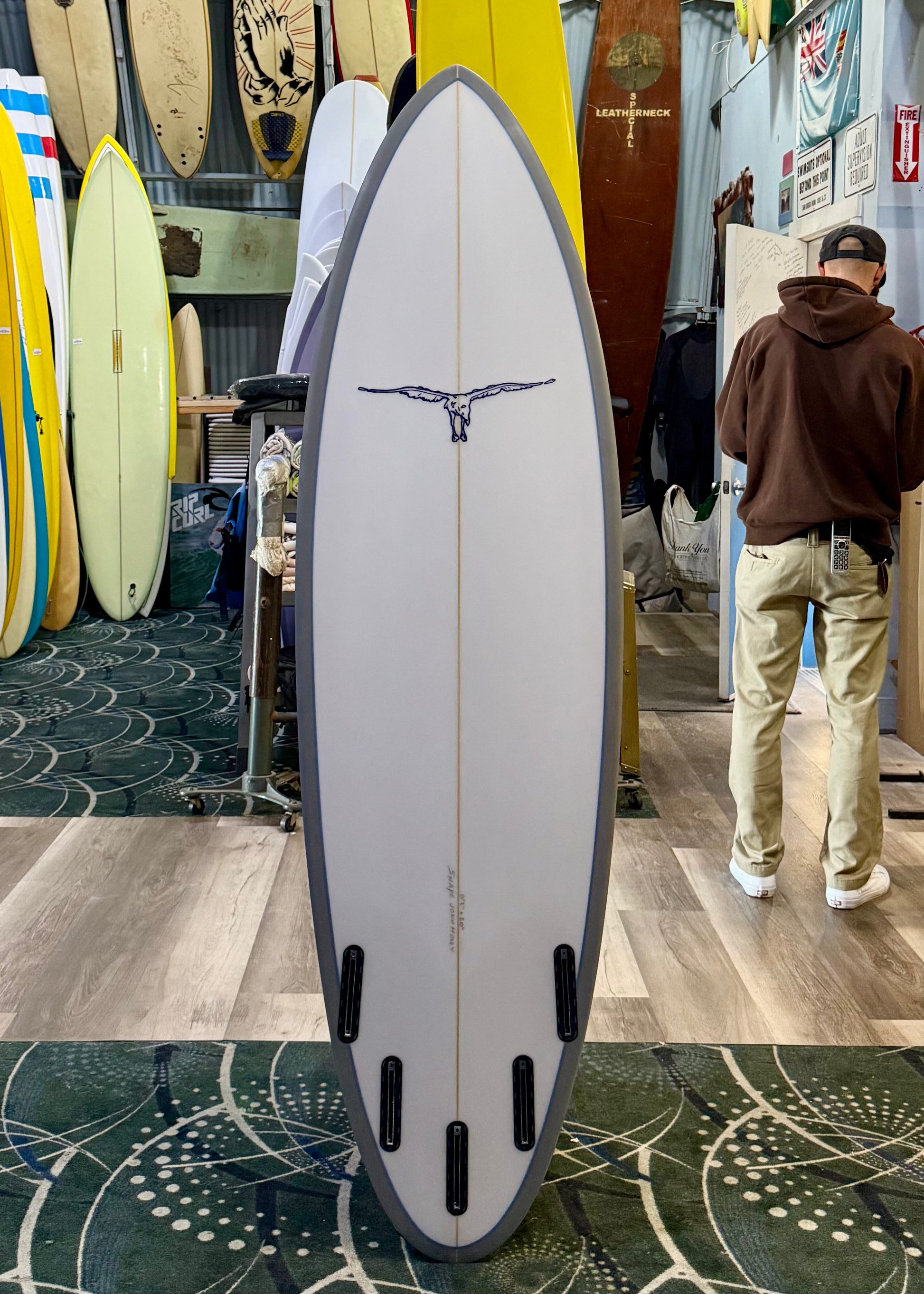 Surfboard with a logo on display in a store with a person in the background.