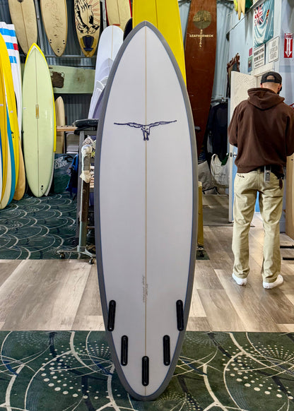 Surfboard with a logo on display in a store with a person in the background.