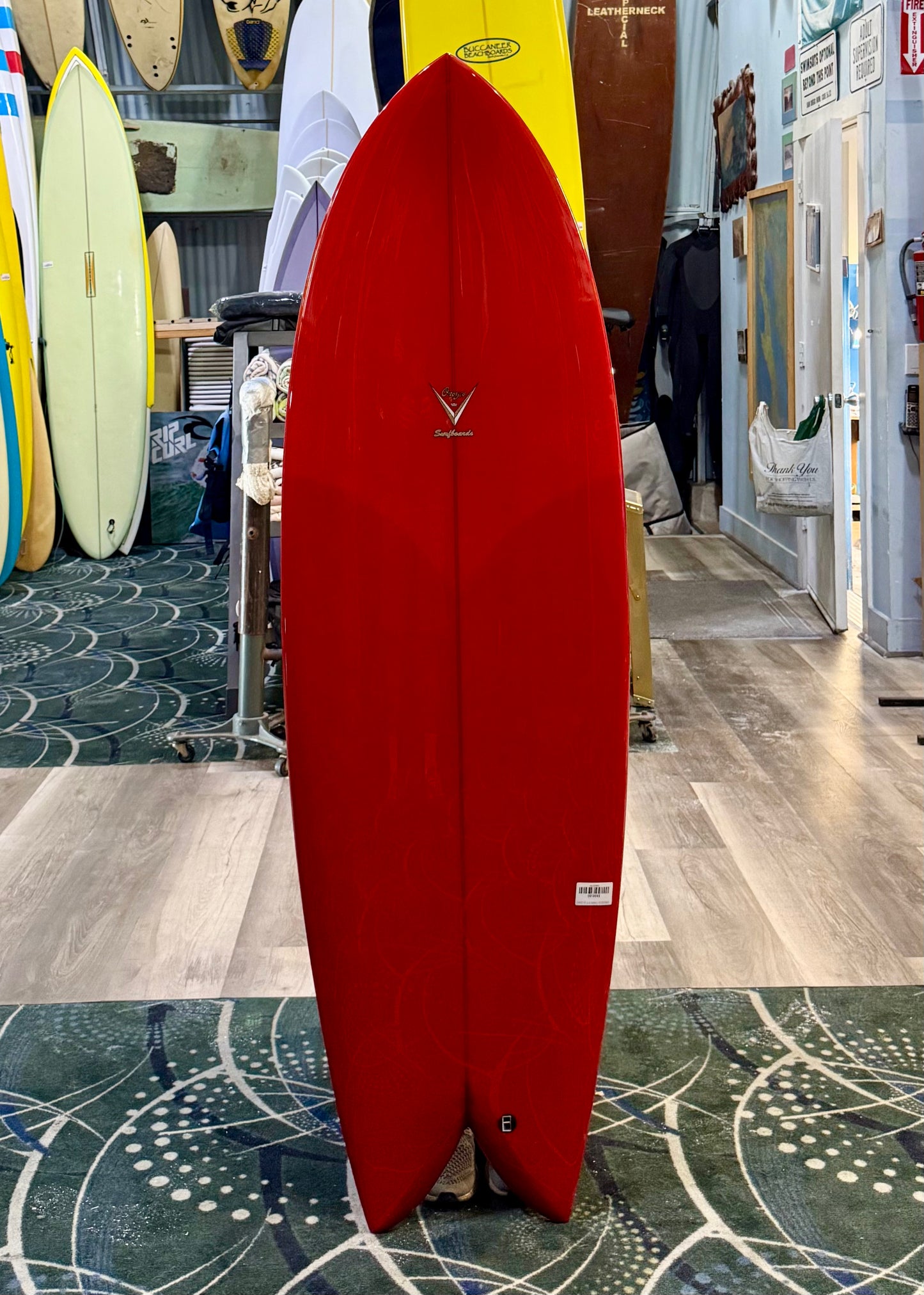 Red surfboard with a logo on display in a store with other surfboards in the background.