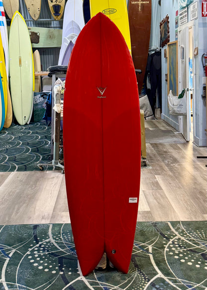Red surfboard with a logo on display in a store with other surfboards in the background.