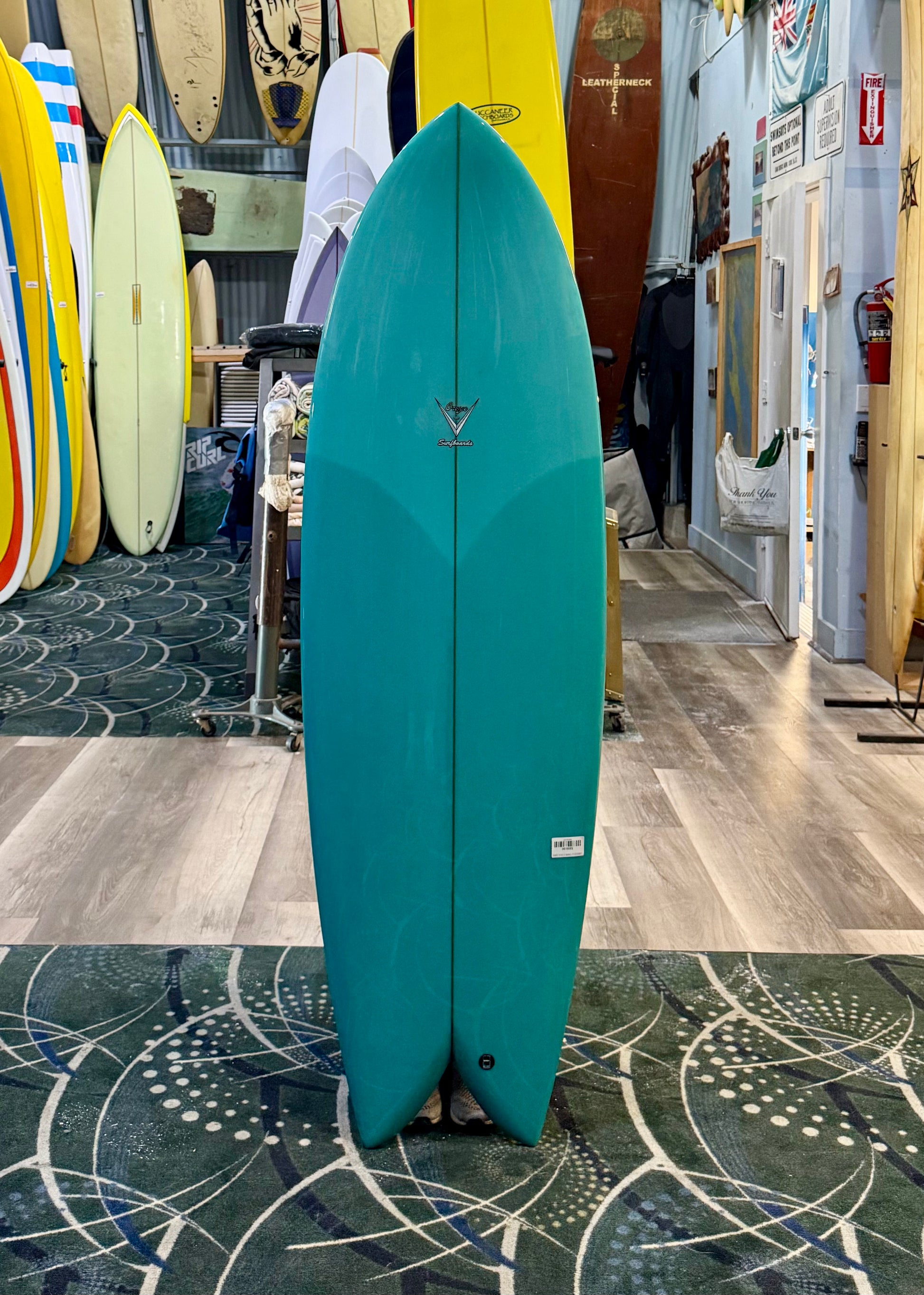 Teal surfboard standing on a patterned floor with surfboards in the background