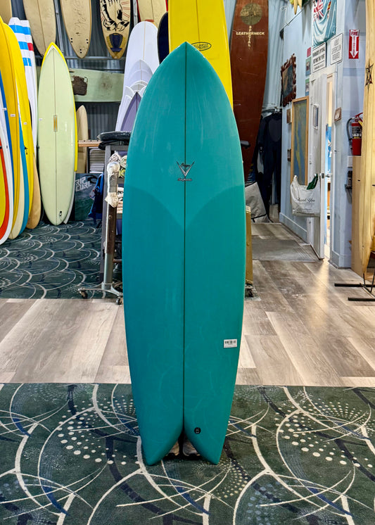 Teal surfboard standing on a patterned floor with surfboards in the background