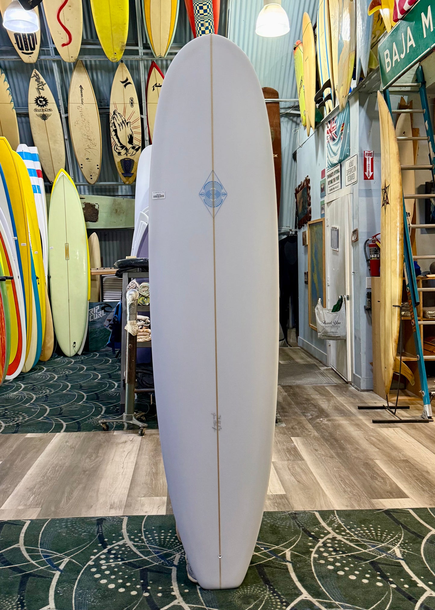 White surfboard with a blue logo in a store with various surfboards and signs on the wall.